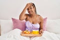 African american woman with braids holding tray with breakfast food in the bed stressed and frustrated with hand on head, Royalty Free Stock Photo