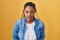 African american woman with braids standing over yellow background afraid and shocked with surprise and amazed expression, fear Royalty Free Stock Photo