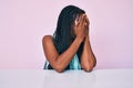 African american woman with braids wearing casual clothes sitting on the table with sad expression covering face with hands while Royalty Free Stock Photo