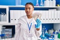 African american woman with braids working at scientist laboratory holding money scared and amazed with open mouth for surprise, Royalty Free Stock Photo