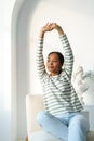 Young african-american female stretching while sitting. Thougtfuly looking at window in morning