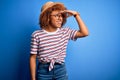 African American woman with curly hair on vacation wearing summer hat and striped t-shirt very happy and smiling looking far away Royalty Free Stock Photo