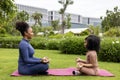 African American woman and her daughter in yoga suit are relaxingly practicing meditation exercise in the park to attain happiness