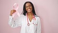 African american woman doctor holding breast cancer awareness pink ribbon over isolated pink background Royalty Free Stock Photo