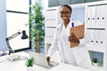 African american woman doctor using laptop holding medical report at clinic Royalty Free Stock Photo