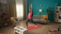 An African American woman doing forward lunges with her arms raised above her head. A young woman watches a video lesson