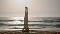 Woman doing headstand yoga pose on seashore at sunrise. Girl training balance.