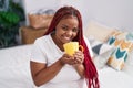 African american woman drinking cup of coffee sitting on bed at bedroom Royalty Free Stock Photo