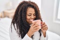 African american woman drinking cup of coffee sitting on bed at bedroom Royalty Free Stock Photo