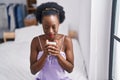 African american woman drinking cup of coffee sitting on bed at bedroom Royalty Free Stock Photo