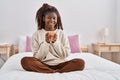 African american woman drinking cup of coffee sitting on bed at bedroom Royalty Free Stock Photo