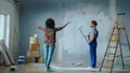 African American woman is giving directions to male house painter painting wall with white paint using long paint roller Royalty Free Stock Photo