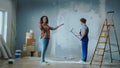 African American woman is giving directions to male house painter painting wall with white paint using long paint roller Royalty Free Stock Photo