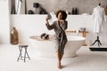 African american woman with golden patches on eyes looks in the mirror. Morning beauty routine. African girl in bathrobe