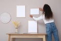 African American woman hanging empty frame on pale rose wall over table in room, back view. Mockup for design Royalty Free Stock Photo