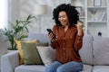 African american woman happy received online notification, good news in notification, woman sitting at home on couch in Royalty Free Stock Photo