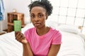 African american woman holding birth control pills sitting on bed at bedroom Royalty Free Stock Photo