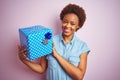 African american woman holding birthday gift over pink isolated background with a happy face standing and smiling with a confident Royalty Free Stock Photo