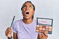 African american woman holding blush palette of nudes colors angry and mad screaming frustrated and furious, shouting with anger