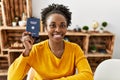 African american woman holding deutchland passport sitting on table at home Royalty Free Stock Photo