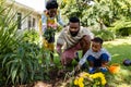 African american woman holding flowers while father and son digging dirt on grassy land in yard Royalty Free Stock Photo