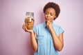 African american woman holding jar of chocolate chips cookies over pink isolated background serious face thinking about question,