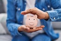 African american woman holding piggy bank sitting on sofa at home Royalty Free Stock Photo