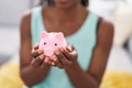 African american woman holding piggy bank sitting on sofa at home Royalty Free Stock Photo