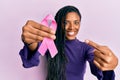 African american woman holding pink cancer ribbon smiling happy pointing with hand and finger