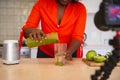 African american woman in kitchen pouring health drink, making vlog using laptop and camera