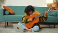 African American woman learning guitar watching tutorial on laptop at home. Black girl playing guitar singing song