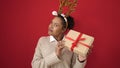 African american woman listening sound christmas gift wearing reindeer ears over isolated red background