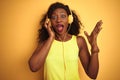 African american woman listening to music using headphones over isolated yellow background very happy and excited, winner Royalty Free Stock Photo