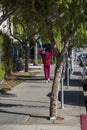 An African American woman with long hair wearing a red sweat suit walking along a sidewalk lined with lush green trees