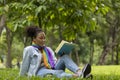 African American woman is lying down in the grass lawn inside the public park holding book in her hand during summer for reading Royalty Free Stock Photo