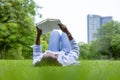 African American woman is lying down in the grass lawn inside the public park holding book in her hand during summer for reading Royalty Free Stock Photo