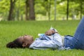 African American woman is lying down in the grass lawn inside the public park holding book in her hand during summer for reading Royalty Free Stock Photo