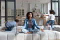 African American woman meditating while noisy kids jumping on couch