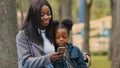 African American woman mother with child daughter little kid girl small baby schoolgirl sitting in park outdoors Royalty Free Stock Photo