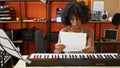 African american woman musician playing piano reading music sheet at music studio