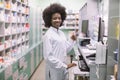 African-american woman pharmacist on her workplace in modern drugstore, standing near the counter with computer and Royalty Free Stock Photo