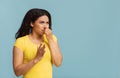 African american woman plugging her nose, smelling something stinky and unpleasant on blue background, copy space