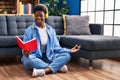 African american woman reading book doing yoga exersice sitting on floor at home