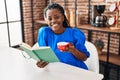 African american woman reading book and drinking coffee at home Royalty Free Stock Photo