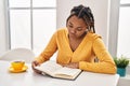 African american woman reading book and drinking coffee sitting on table at home Royalty Free Stock Photo