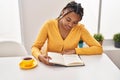 African american woman reading book and drinking coffee sitting on table at home Royalty Free Stock Photo