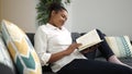 African american woman reading book sitting on sofa at home Royalty Free Stock Photo