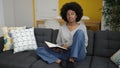 African american woman reading book sitting on sofa at home Royalty Free Stock Photo