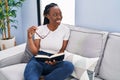 African american woman reading book sitting on sofa at home Royalty Free Stock Photo