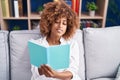 African american woman reading book sitting on sofa at home Royalty Free Stock Photo